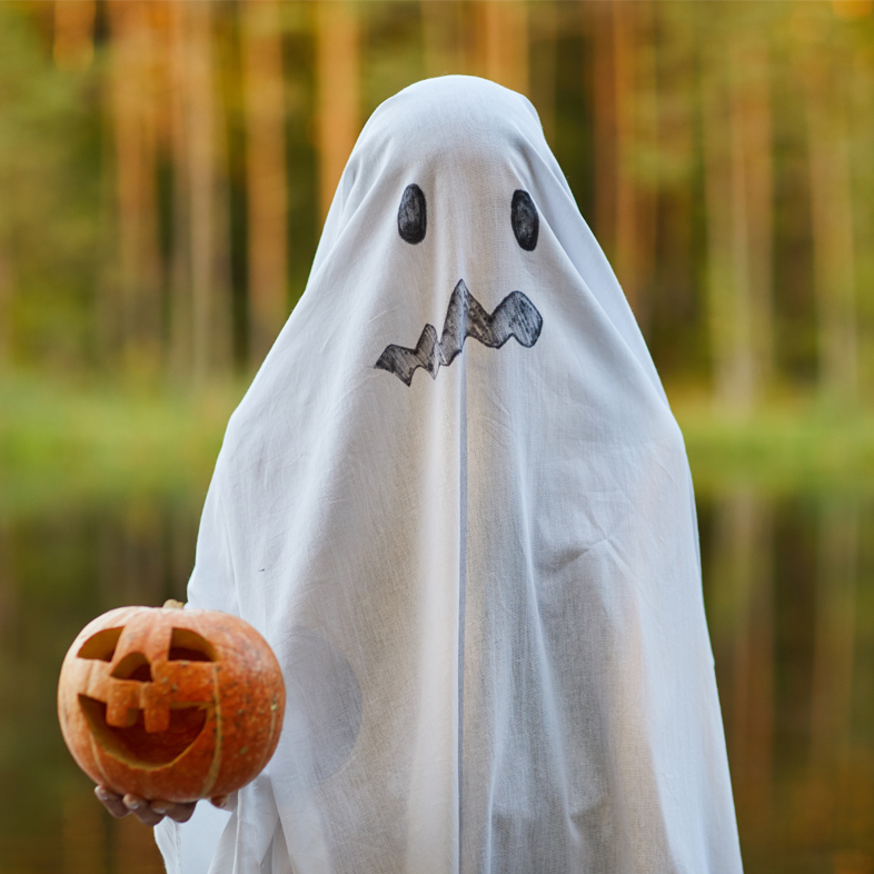 Person in ghost costume holding a pumpkin