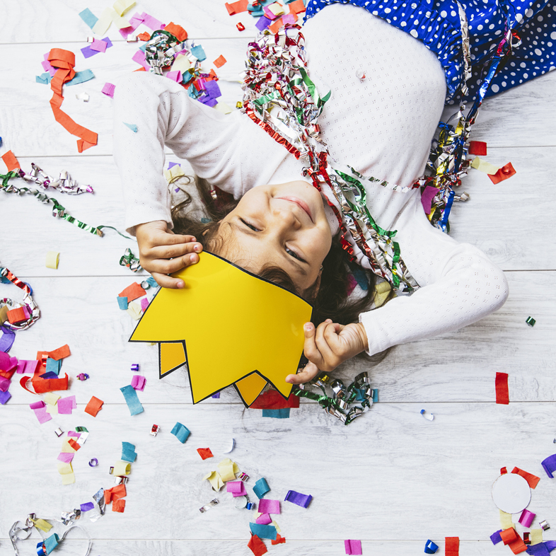 Girl laying on floor with confetti and paper crown