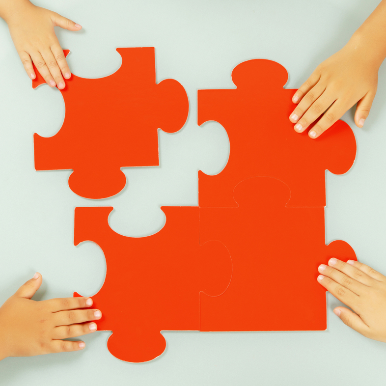 Four hands putting four puzzle pieces together