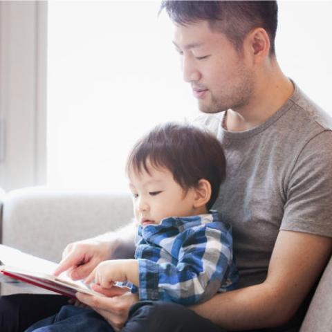 Person reading to toddler on couch